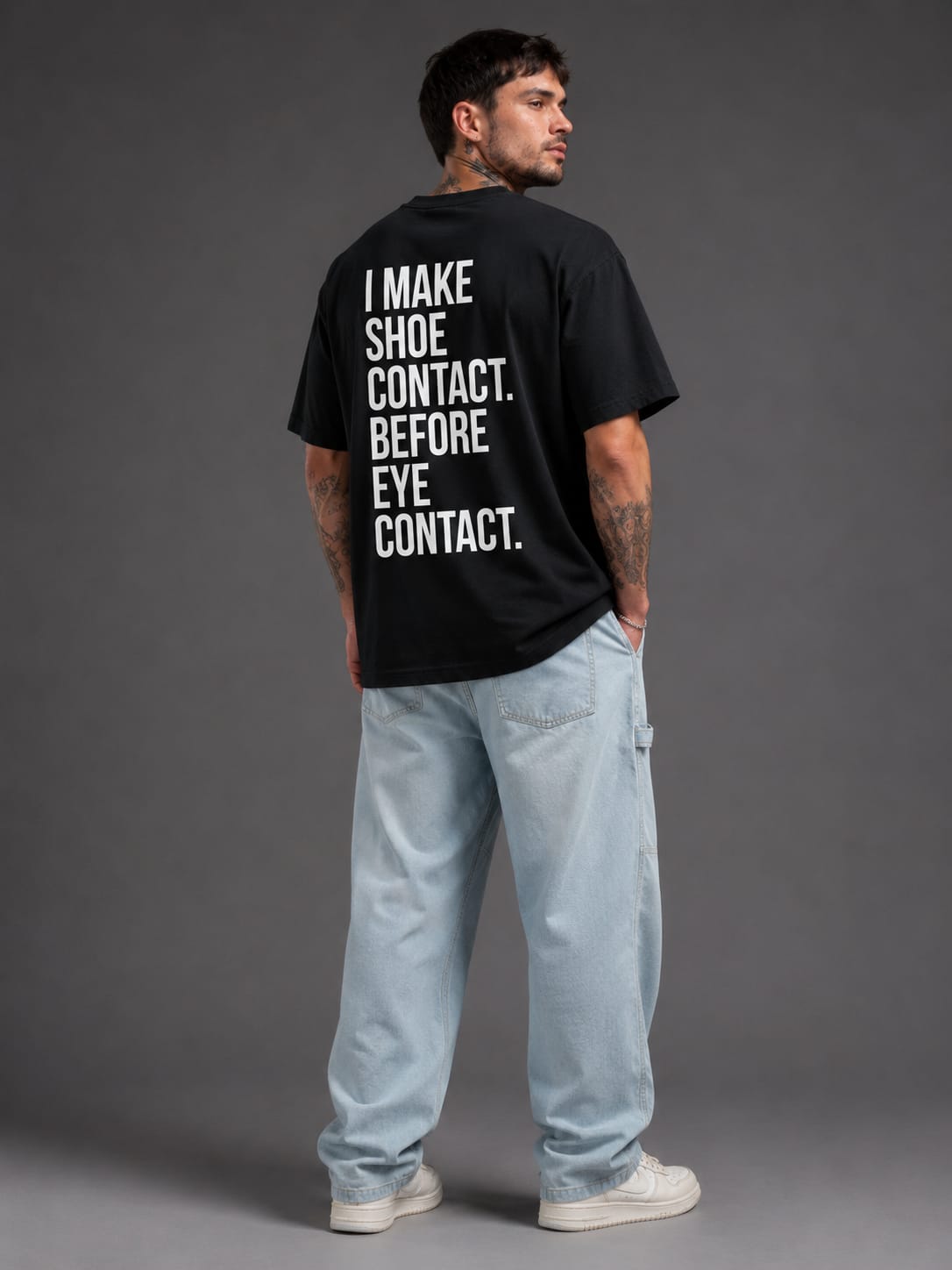 Male model showcasing the back graphic of the SNKR HEAD oversized off black t-shirt.